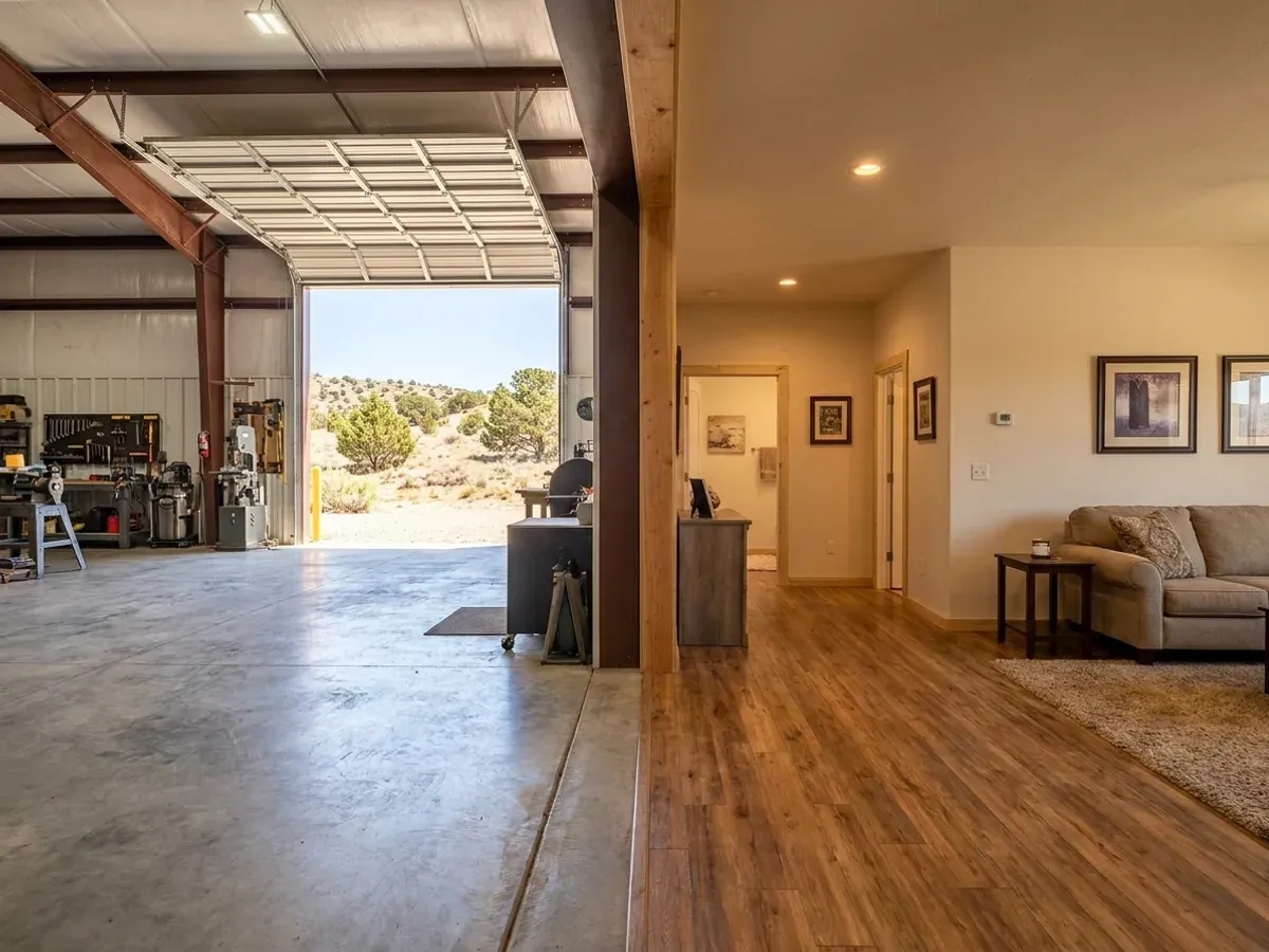 The interior of a shouse where a finished living area with warm flooring meets a shop bay with polished concrete and a tall open roll-up door.
